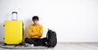 Displeased traveler guy with bad expression sits with suitcase isolated on white background
