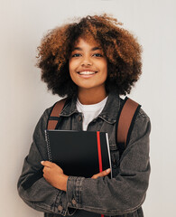 Wall Mural - Cheerful girl with curly hair holding a books wearing backpack