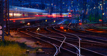 Panorama At Main Station Of Hagen In Westphalia Germany At Blue Hour Twilight. Railway Tracks With Switches, Lamp Lights And Blurred Trains In Motion. Colorful Railway Infrastructure And Technology. 