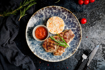 Canvas Print - Pork steak with rice and tomato sauce on plate on dark table top view