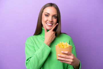 Wall Mural - Young caucasian woman holding fried chips on purple background happy and smiling