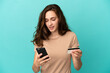 © luismolinero - Young caucasian woman isolated on blue background buying with the mobile with a credit card