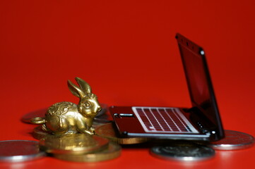 Wall Mural - A rabbit figurine with coins and a laptop on a red background. Financial symbol. Business strategies.