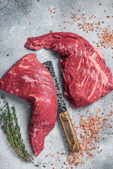 Wall Mural - Unccoked tri-tip triangle roast, raw bottom sirloin steak on buther table with meat cleaver. Gray background. Top view