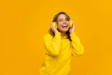 Wall Mural - smiling attractive woman listening to music in headphones on yellow background
