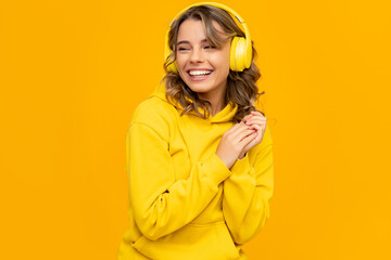 Wall Mural - smiling attractive woman listening to music in headphones on yellow background