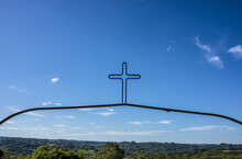 Decorative Metal Cross Against A Blue Sky With Green Landscape; Pelotas, Rio Grande Do Sul, Brazil