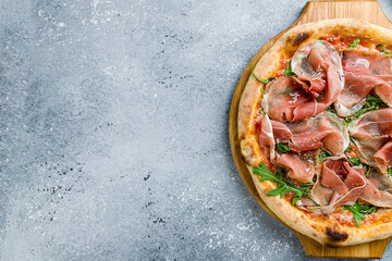 Canvas Print - Pizza with Parma ham and arugula on wooden board on grey table top view with copy space