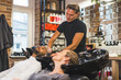 © PoppyPix - Happy indian male client having his hair washed with shampoo by hairdresser next to blonde female customer in a professional hair salon. High quality photo