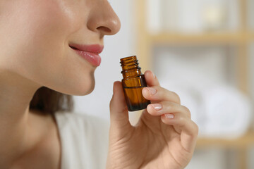 Wall Mural - Young woman smelling essential oil on blurred background, closeup. Space for text