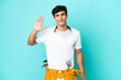 © luismolinero - Young electrician Argentinian man isolated on blue background saluting with hand with happy expression