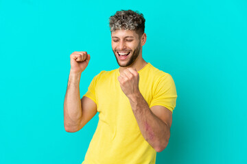 Young handsome caucasian man isolated on blue background celebrating a victory