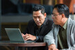 © amorn - Two Asian businessmen using laptop computer working, talking, sharing ideas, discussing planing in modern office. business, people, office concept