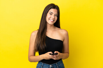 Wall Mural - Young Brazilian woman isolated on yellow background sending a message with the mobile