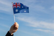 © yta - Australian flag in hand flutters in the wind against the sky, independence national day of Australia, country freedom, patriotism, Public Holiday, patriotic festival