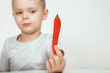 Little boy with chili pepper on white background. Extra hot cayenne pepper. Boy holding spicy red chili pepper. Portrait of a shocked kid.
