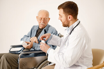 Wall Mural - Male doctor and old man on a wheelchair isolated on a white background