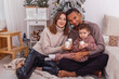 © Natasha  - A young diverse family with a baby boy is sitting with candle near a Christmas tree
