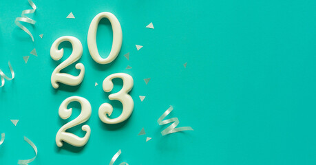 Wall Mural - close up number 2023 shape wood on blue color background with rolling ribbon and confetti for happy 