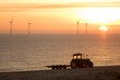 Misty morning sunrise. Beach tractor with offshore wind farm turbines. Eco landscape image for environmental conservation.