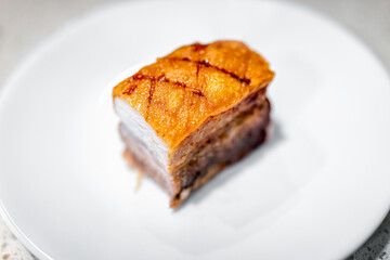 Wall Mural - Macro closeup flat top flay lay view of cut fresh barbecue cooked baked fried pork belly fat bacon meat with crispy crunchy skin, nutritious food isolated against white plate at kitchen table