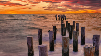 wooden pier or jetty on the beach at sunset and stunning reflections in the water. long exposure nea