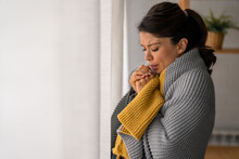 Woman Breathing On Her Hands To Keep Them Warm. Woman Standing By The Window Covered With Plaid Warming Up Hands With Breath In A Cold Apartment. It's Cold Inside. Central Heating Problems Concept.