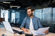 © Liubomir - Mature businessman in shirt doing paperwork, man working with documents, contracts and bills sitting at table using laptop at work, financier accountant with beard and glasses.