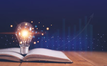 Light Bulb On Open Book With Growing Graphs Of Stock Market, Educational Knowledge And Business Education Concepts, Reading For Inspiration And New Idea To Business Grow In The Future.