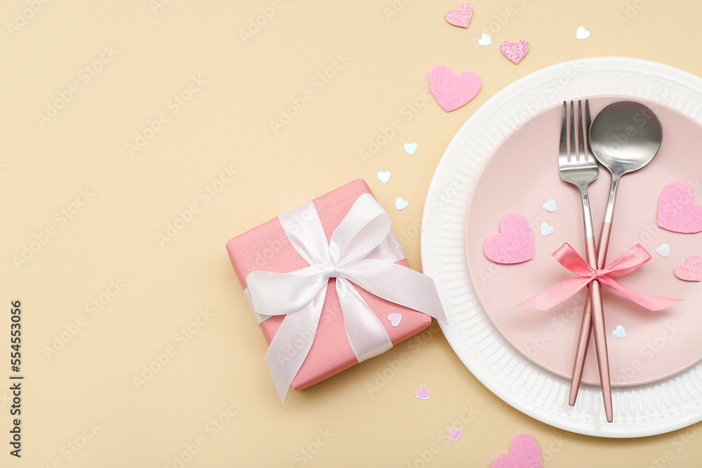Table setting for Valentine's Day with pink hearts and gift on beige background