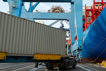 Wall Mural - Port container terminal with container ship in background and white container in foreground