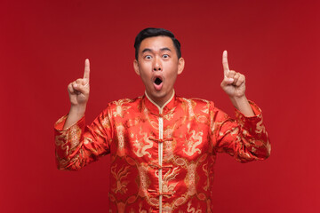 Young asian man wearing Chinese red shirt with hand point to copy space on red background for Chinese new year festival