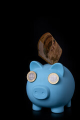 Blue piggy bank with coins in denominations of 100 Kazakhstani tenge on a black background