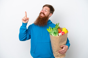 Wall Mural - Redhead man with beard holding a grocery shopping bag isolated on white background pointing up a great idea