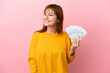 © luismolinero - Redhead girl taking a lot of money isolated on pink background looking to the side and smiling