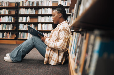 Poster - Library, college student and black woman reading books on ground floor for education, studying and campus learning. University student, girl and bookshelf for project, knowledge and academy research