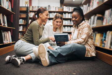 Poster - Books, education and friends on a library floor for learning, research and homework assignment, happy and excited. Campus, women and university students bond on ground with book for exam preparation