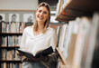 © Kay A/peopleimages.com - Student, reading or books in library on school, university or college campus for education, study research or learning. Portrait, smile or happy woman, textbook or bookshelf information for homework