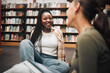© K Abrahams/peopleimages.com - University, students and friends on library floor for studying, education and learning together. Happy black girl, gen z youth and college student at academy, campus and school in room with bookshelf