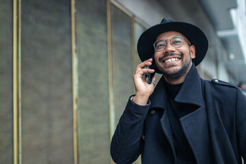 Wall Mural - elegant latin man on the street walking smiling talking on mobile phone wearing hat