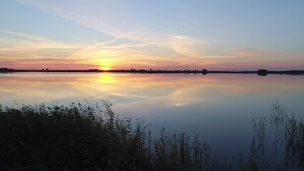 Wall Mural - Aerial over the lake at sunset. Soft sunset skies reflections on calm water surface. Stunning summer scenery