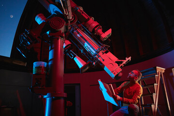 Wall Mural - astronomer with a big astronomical telescope in observatory doing science research of space and cele