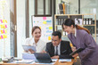 © PHAISITSAWAN - Team business three smiling and happy Asian men and women team using tablets and laptops brainstorm and plot statistics on a corporate chart board inside the company. Colleagues concept.