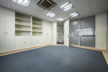 Empty coworking office with gray walls, wooden shelves and glass partitions, a technical ceiling and a blue carpet floor