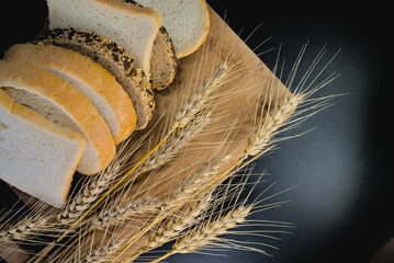 Slices of bread and ears of wheat on black background