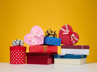 Wall Mural - A stack of gift boxes wrapped in colorful paper on a yellow background. Happy Holidays