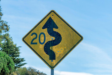 Aged and weathered curvy or windy road sign suggesting to keep speed at twenty miles per hour