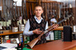 © JackF - Salesman standing behind counter at gun store, showing double barreled hunting rifle