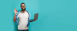 © San4ezz007 - Young bearded charismatic man hipster. Shocked or surprised expression. Laptop concept. Promotion poster. Programmer, web developer holding a laptop in his hands and looking at the camera