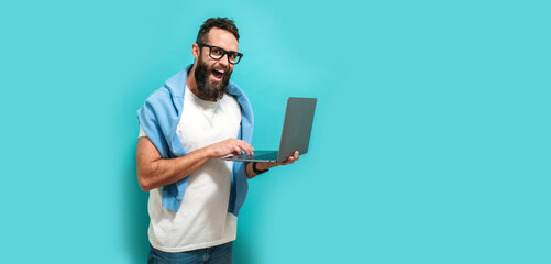 Wall Mural - Young bearded charismatic man hipster. Shocked or surprised expression. Laptop concept. Promotion poster. Programmer, web developer holding a laptop in his hands and looking at the camera